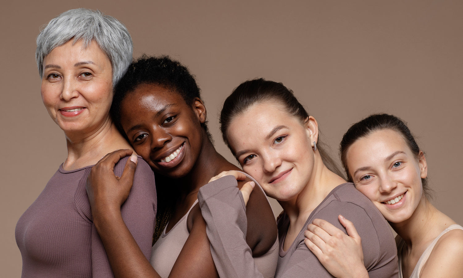 Quatro mulheres de diferentes idades e etnias abraçadas, representando diversidade e longevidade da pele em todas as fases da vida