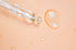 pipeta e uma gota de sérum de skincare em um fundo cor de pêssego