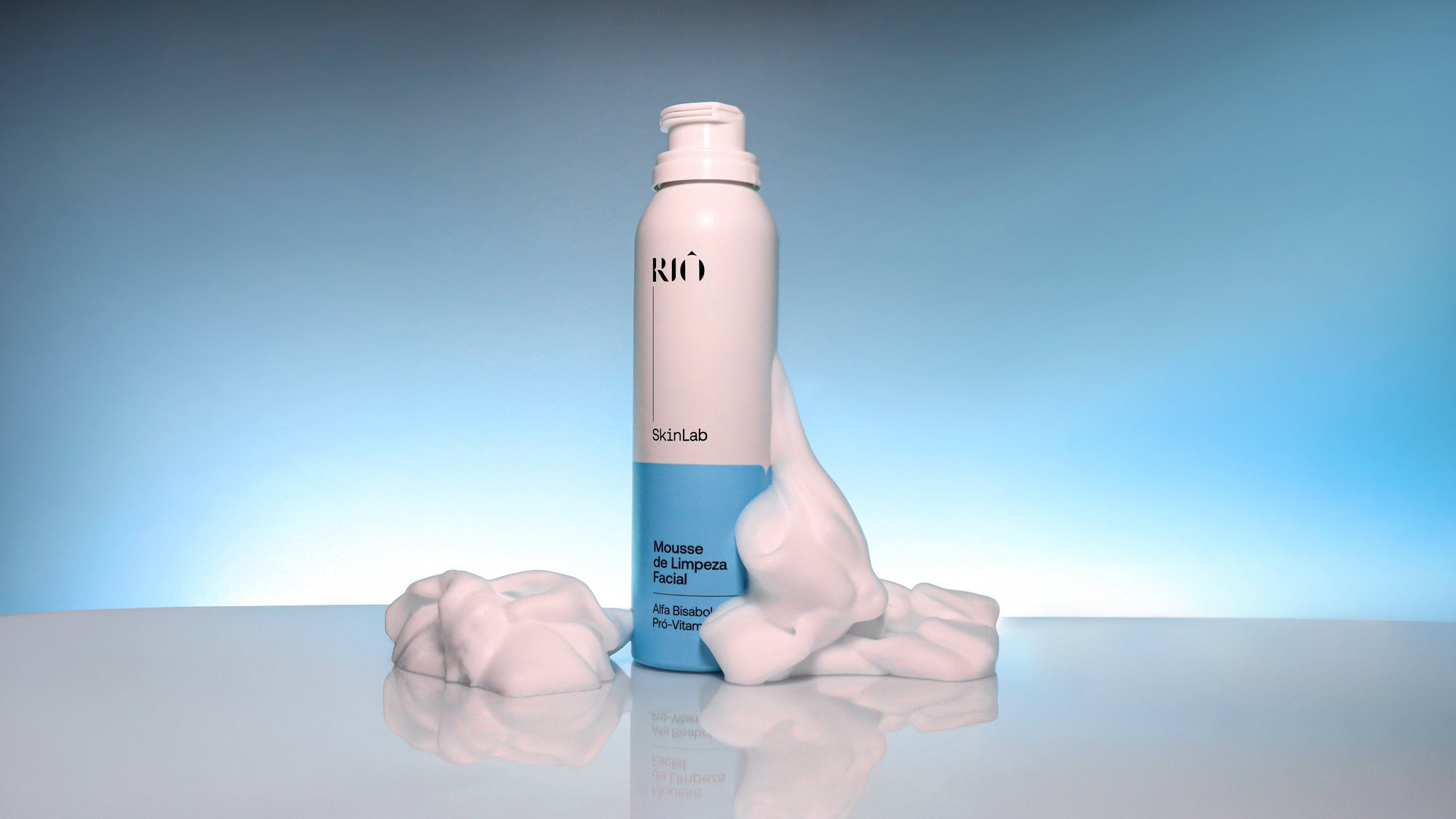 Frasco da Mousse de Limpeza Facial Riô cercado por espuma branca sobre fundo azul claro.